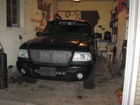 2003 Ford Ranger - A black Ford Ranger is parked inside a cluttered garage, showing its front grille and headlights.