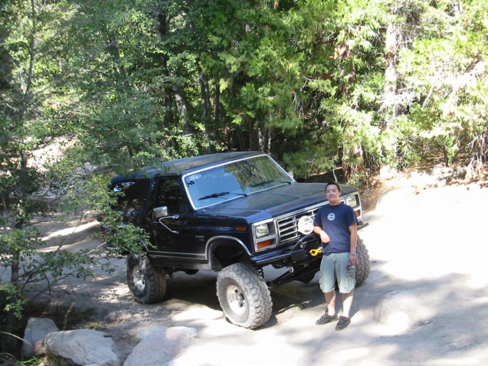 Lifted dark Ford Bronco SUV on rocky trail with man standing beside it