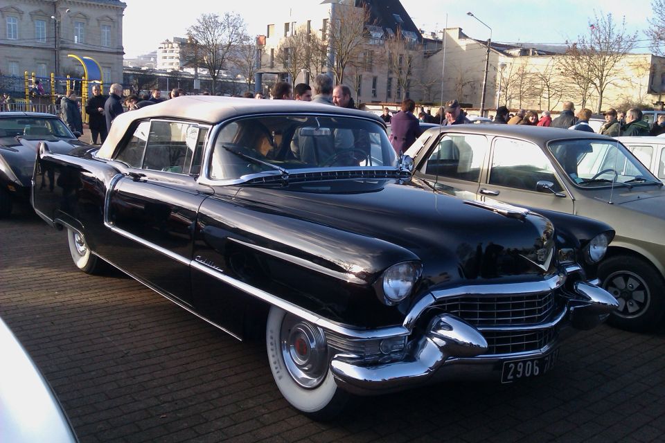 Black 1955 Cadillac convertible with white top, parked next to a tan sedan