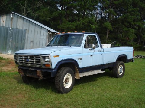 1984 Ford F-250 - This light blue 1980s Ford F-250 pickup truck is parked on a grassy area next to a metal building.