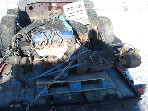 1977 Ford F-150 - Various vehicle parts, including an engine and tires, are secured on a trailer for transport.