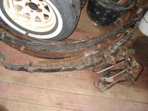 1977 Ford F-150 - A collection of vehicle leaf springs and a tire are piled on a wooden floor.