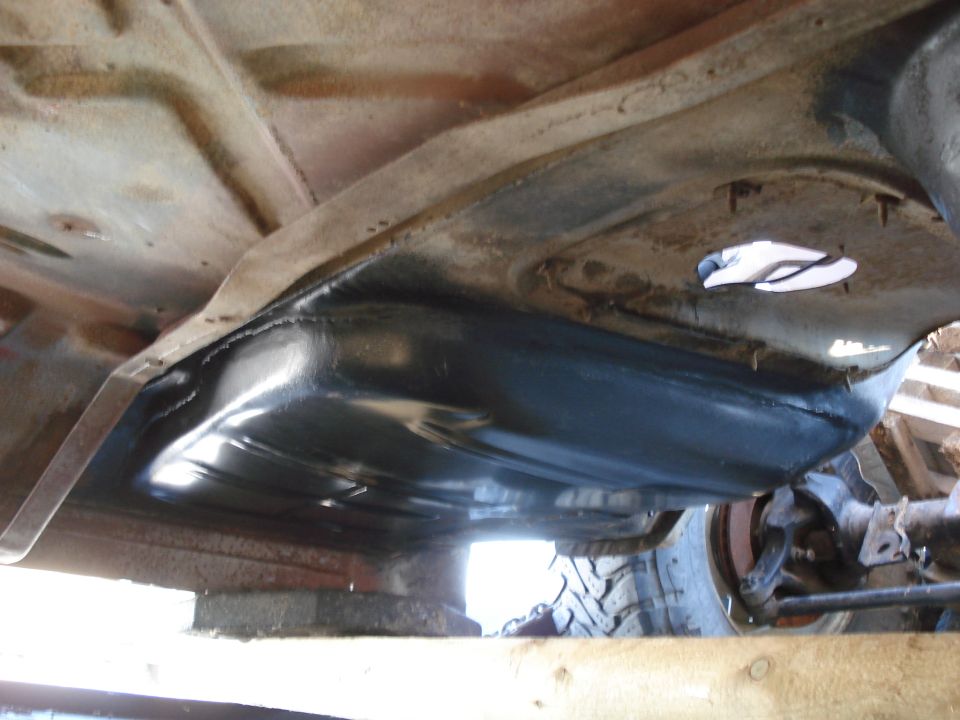 Underside view of a vehicle's fuel tank and frame rails, with a tire visible