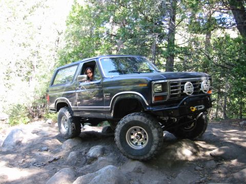 1985 Ford Bronco - Ford Bronco tackles a challenging rocky path in a wooded area.