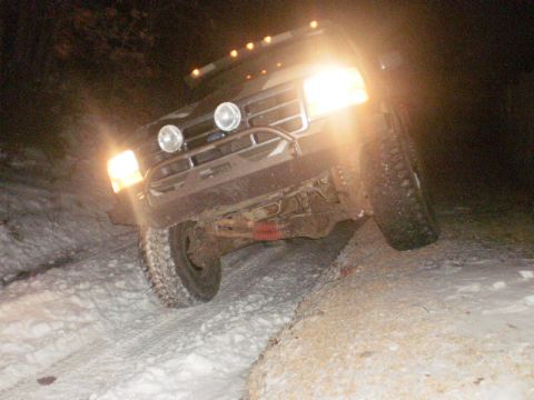 1995 Ford Bronco - 1995 Ford Bronco navigating a snowy path at night with its lights illuminating the way.