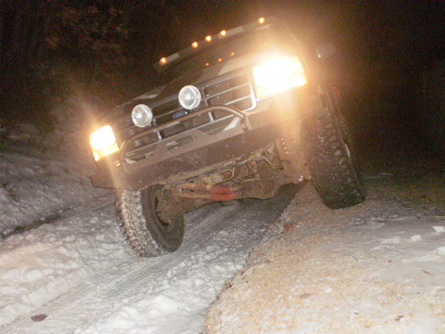 1995 Ford Bronco driving on a snowy road at night with headlights on