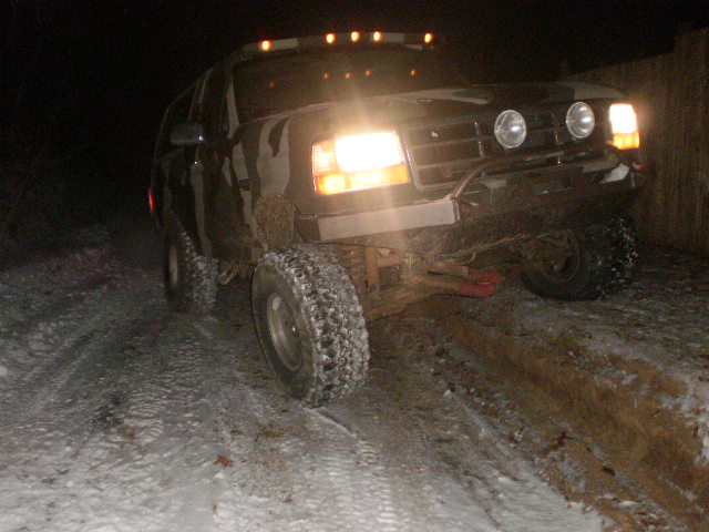 Ford F-Series truck with aftermarket lights on the roof, driving on a snowy dirt road at night