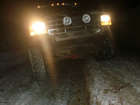 1995 Ford Bronco - A black Ford Bronco navigates a snowy path at night, its headlights illuminating the way.