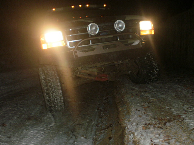 Black Ford Bronco with aftermarket bumper and auxiliary lights, front view, driving in snow