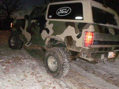 1995 Ford Bronco - Rear view of a 1995 Ford Bronco with camouflage paint, parked on snowy terrain.
