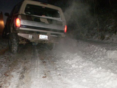 1995 Ford Bronco - A Ford Bronco navigates a snowy path at night, its taillights illuminated and exhaust visible.