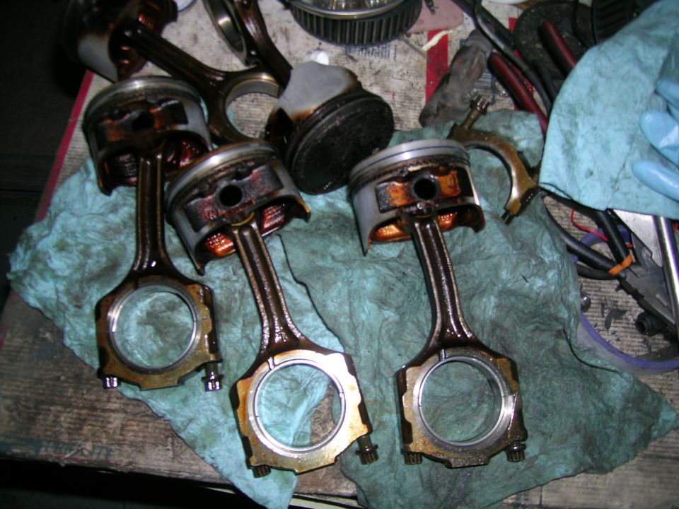 Several engine pistons with connecting rods attached, resting on a blue cloth. Some appear dirty and used