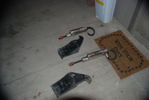 1982 Ford Bronco - Parts laid out on the ground, including shock absorbers and metal brackets, with a doormat nearby.
