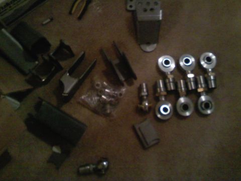 1990 Ford Bronco - Various metal automotive parts, including rod ends and fasteners, are laid out on a textured surface.