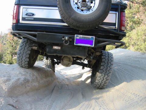 1985 Ford Bronco - This black Ford Bronco is shown from the rear, navigating a rocky and sandy off-road trail.