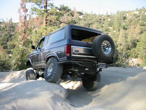 1985 Ford Bronco - This 1985 Ford Bronco navigates a challenging off-road trail with its lifted suspension and large tires.