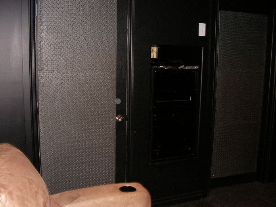Interior room with diamond plate wall panels, a black entertainment unit with shelves, and a tan recliner with a cup holder