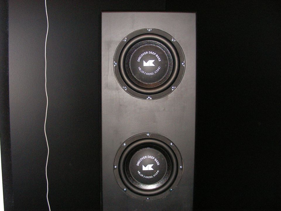 Dual subwoofers in a black cabinet with text 'DISCOVER DEEP BASS MILLER & KRISEL SOUND' on the cones