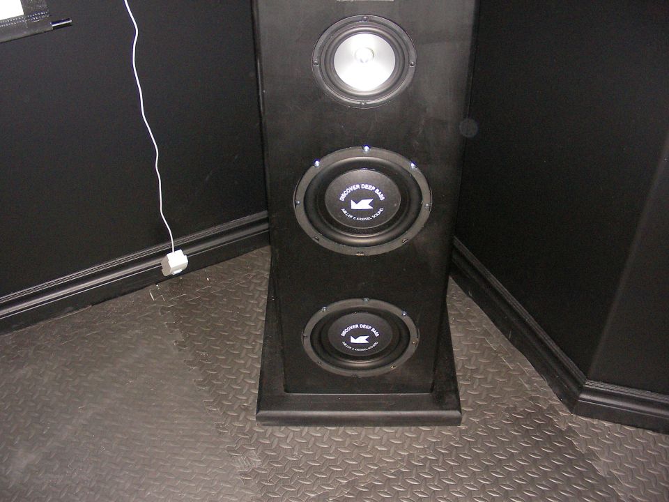 Black speaker cabinet with three drivers, two labeled 'Discover Deep Bass'. White cord plugged into wall