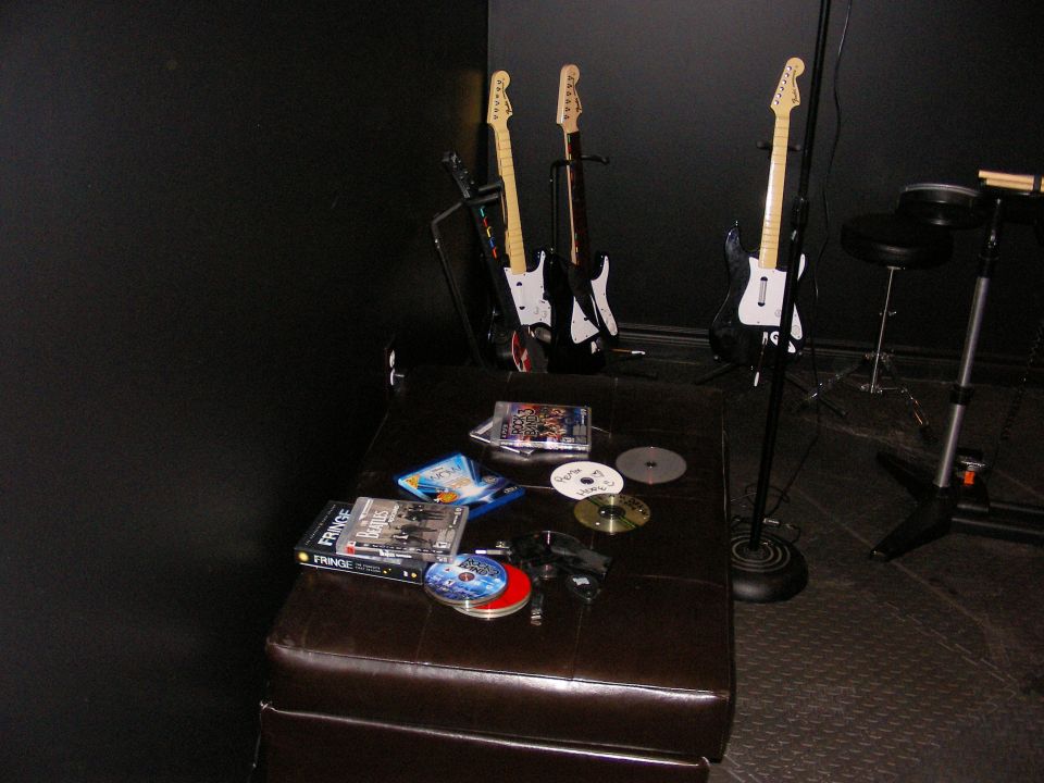 Three electric guitars on stands, plus DVDs and CDs on a dark leather bench