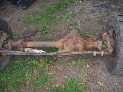 1992 Ford F-150 - A heavily rusted front axle assembly, likely from a truck, lies on the ground.
