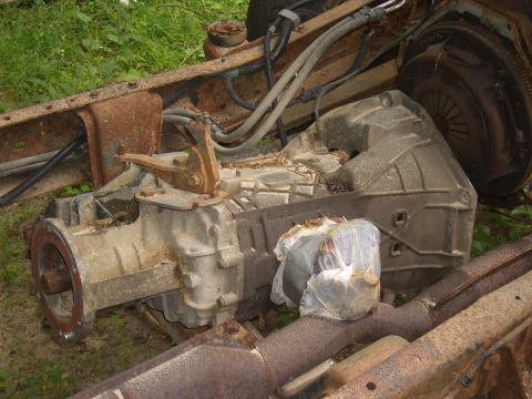 1992 Ford F-150 - A close-up view of a heavily rusted truck frame and transmission assembly, with a plastic-wrapped item obscuring part of the view.
