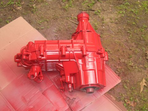 1992 Ford F-150 - A freshly painted red transfer case sits on a piece of cardboard outdoors.