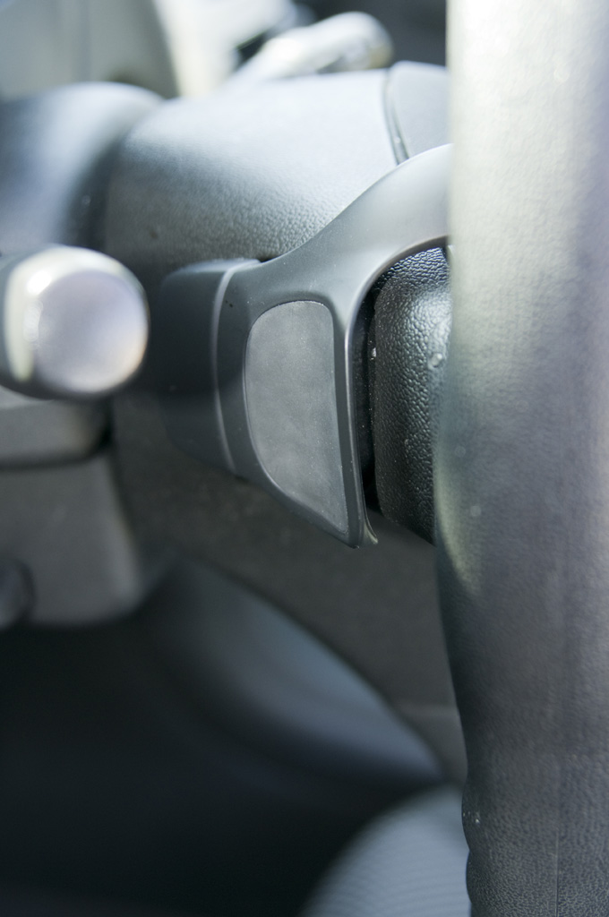 Close-up of a black paddle shifter on a steering column, with a silver stalk visible to the left