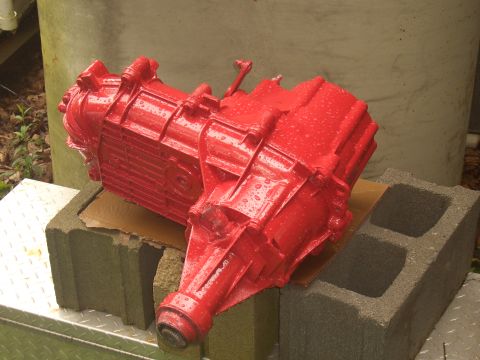 1992 Ford F-150 - A red painted transfer case rests on cinder blocks outdoors, showing water droplets on its surface.