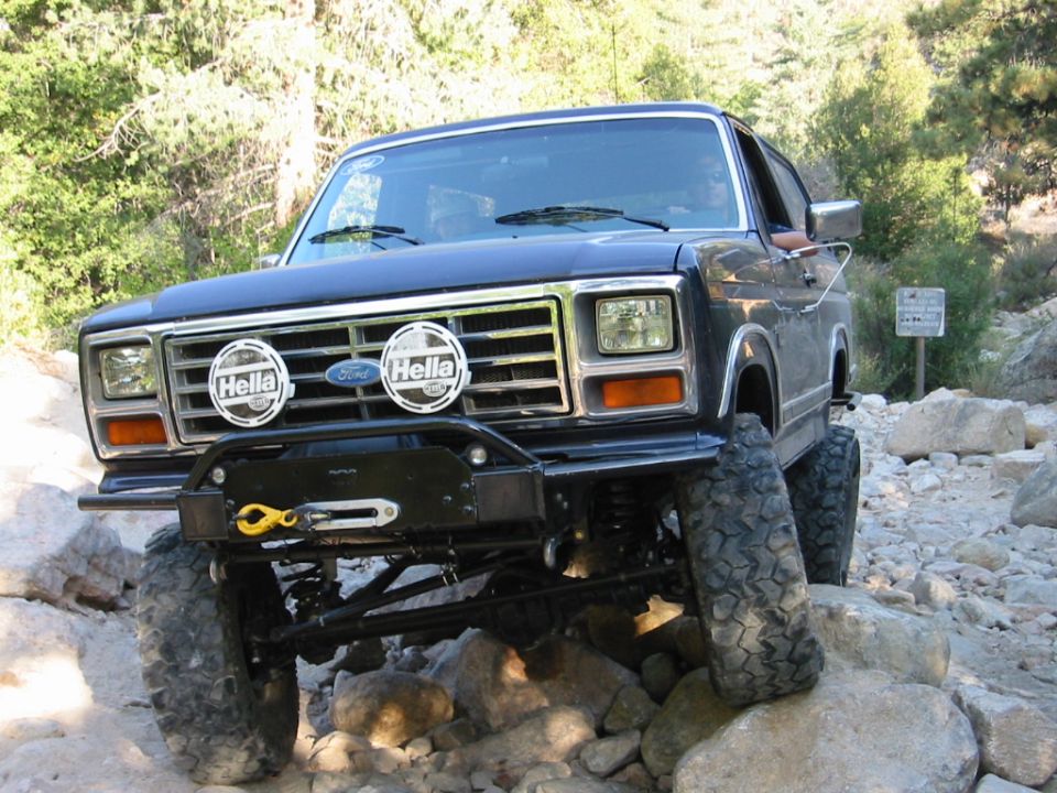 Black lifted Ford Bronco with Hella lights and winch bumper crawling over rocks off-road
