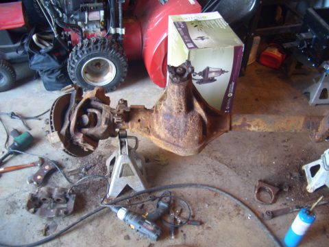 1992 Ford F-150 - A heavily rusted rear axle assembly is supported by jack stands, surrounded by tools and equipment.
