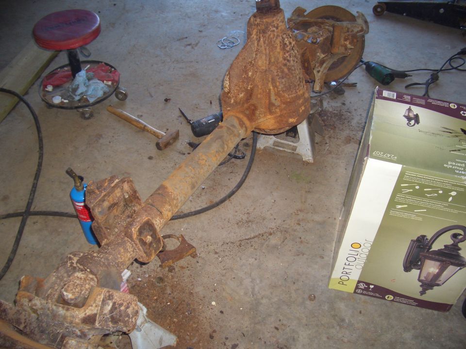 Rusty truck axle assembly on jack stands with tools and a propane torch