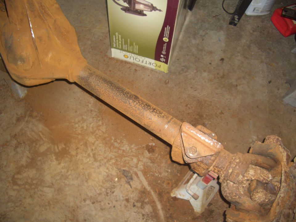 Rusty rear axle assembly on a concrete floor, with a box in the background