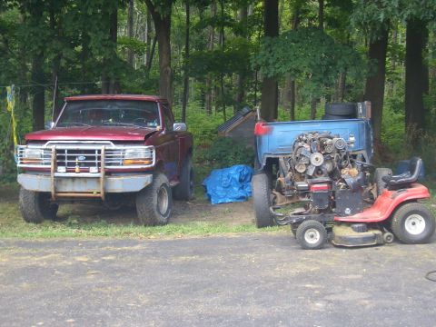 1992 Ford F-150 - A red pickup truck is parked next to a lawnmower that has had a large engine mounted onto it.