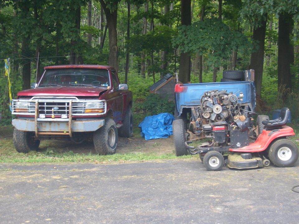 red pickup truck with a big bumper, next to a lawnmower with a large engine installed
