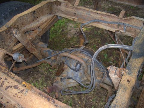 1992 Ford F-150 - The heavily rusted frame and rear axle assembly of a truck are shown, resting on the ground.