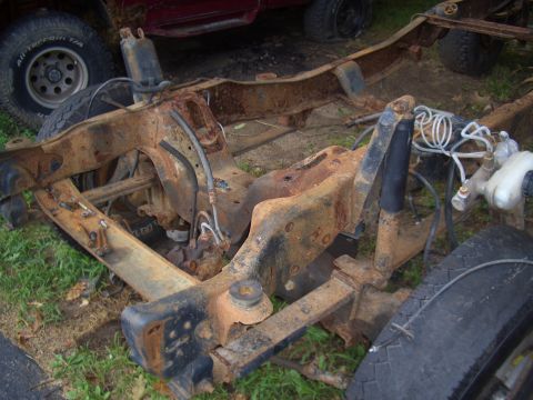 1992 Ford F-150 - A heavily rusted truck chassis is visible, with parts of another vehicle in the background.