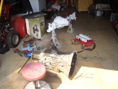 1992 Ford F-150 - Various vehicle transmission and differential components are laid out on the garage floor, with a red Craftsman stool in the foreground.