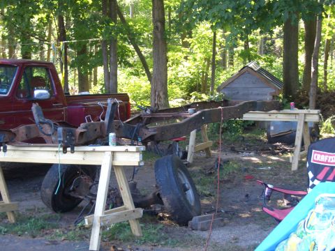 1992 Ford F-150 - The frame of a red pickup truck is disassembled and supported by sawhorses in a wooded area.