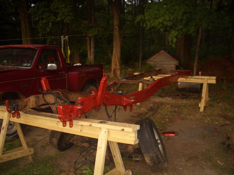 1992 Ford F-150 - The frame of a red truck is supported by sawhorses outdoors, with the truck's cab visible to the left.