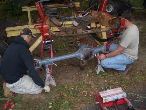 1992 Ford F-150 - Two men are working on a vehicle's frame and rear axle assembly, which is elevated on jack stands.