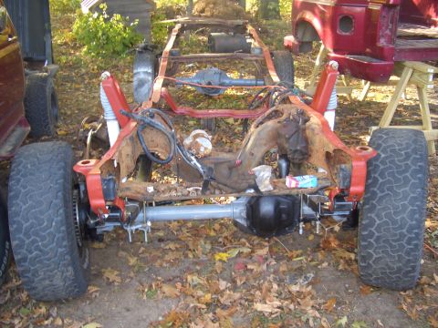 1992 Ford F-150 - The heavily rusted frame of a vehicle sits on the ground outdoors, with parts of another vehicle visible nearby.