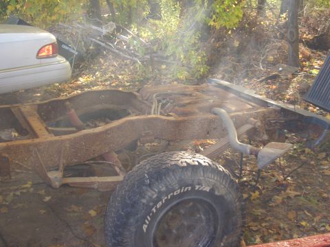 1992 Ford F-150 - Rusted truck frame and parts sit outdoors with autumn leaves on the ground.