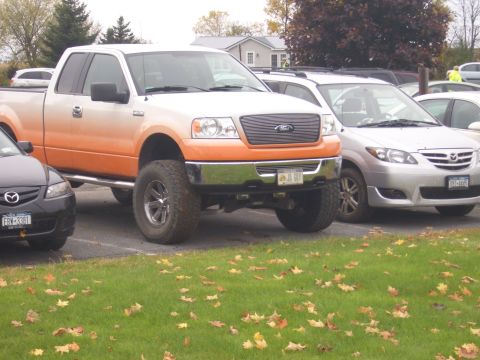 1992 Ford F-150 - A lifted pickup truck with an orange and white two-tone paint job is parked in a lot with other vehicles.