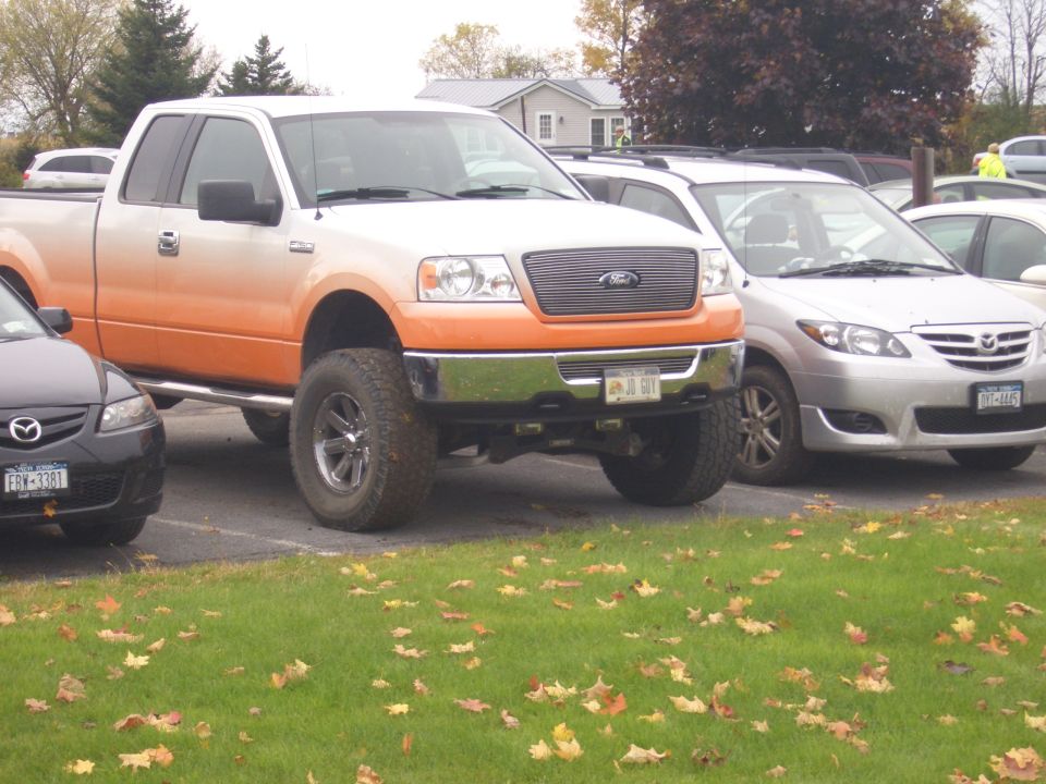 Lifted orange and white pickup truck parked next to a silver Mazda