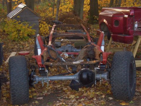 1992 Ford F-150 - The chassis of a disassembled truck sits outdoors with a red cab visible to the right.