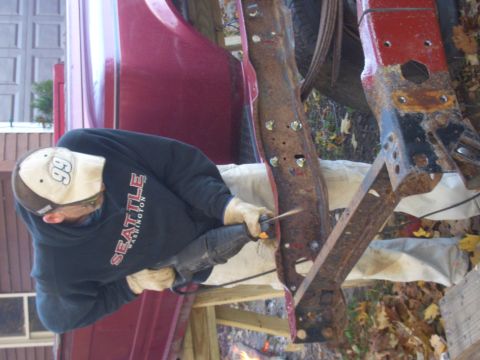 1992 Ford F-150 - A person is using a reciprocating saw to cut into a heavily rusted truck frame, with a red body panel in the background.