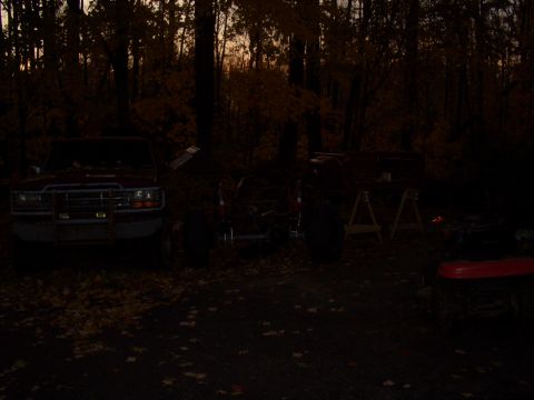 1992 Ford F-150 - A red 1992 Ford F-150 is seen from the front in a dimly lit outdoor setting with trees and fallen leaves.