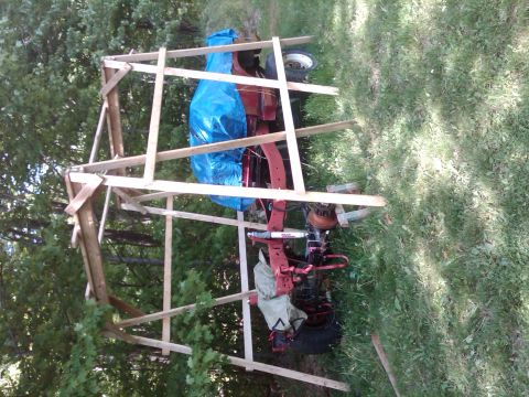 1992 Ford F-150 - A red lawn tractor is partially covered by a blue tarp and situated under a makeshift wooden frame outdoors.