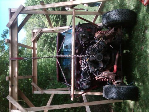 1992 Ford F-150 - The engine and chassis of a truck are suspended by chains within a wooden frame, suggesting a build or repair process.